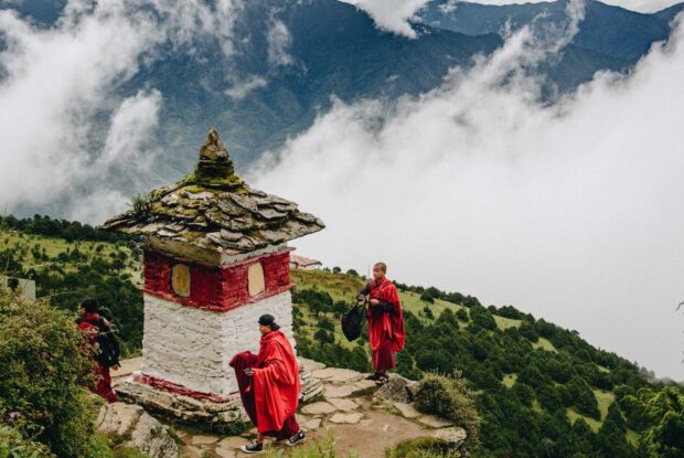Young monks walking near a traditional monument in Bhutan surrounded by mountains and clouds