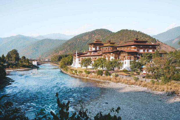 Traditional Bhutan architecture beside a river surrounded by forested mountains in Bhutan