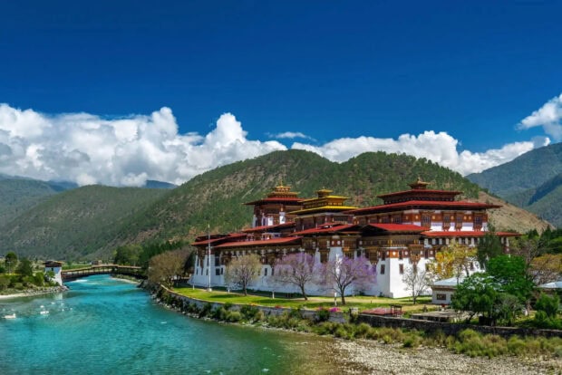 Traditional Bhutan architecture beside a turquoise river with mountains in the background