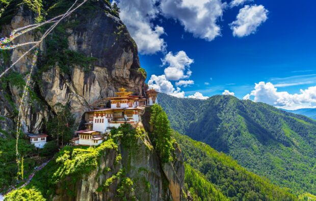 Traditional Bhutan monastery perched on rocky cliff with lush green mountains in the background