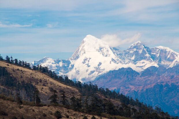 Snow covered mountains in Bhutan landscape with forested hillsides under blue sky