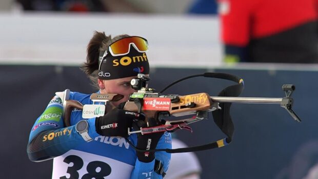 Female athlete aiming with rifle in a biathlon competition wearing blue gear