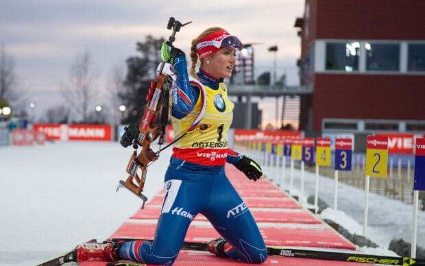 Female biathlon athlete aiming with rifle at shooting range during competition