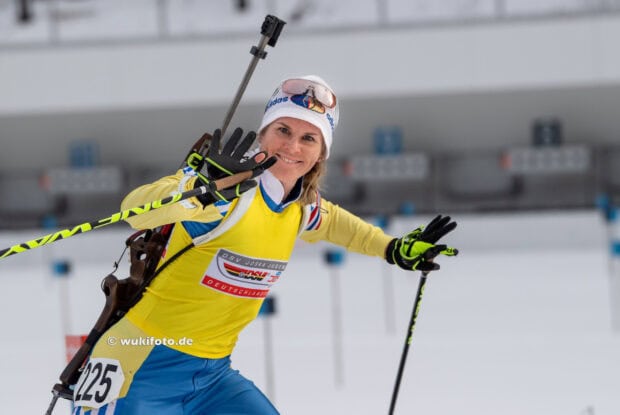 Female biathlon athlete smiling and waving during winter sports event