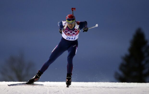 Male athlete competing in biathlon skiing race on snow in winter environment