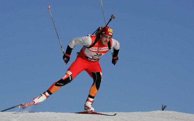 Male biathlon athlete skiing on snow wearing a red suit