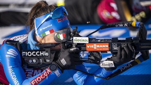 Biathlon athlete aiming with rifle during competition in blue uniform