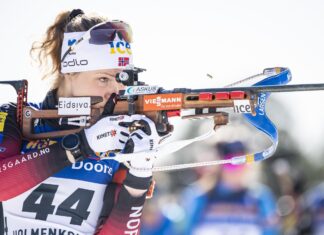 Female biathlon athlete aiming with rifle during competition