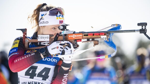 Female biathlon athlete aiming with rifle during competition