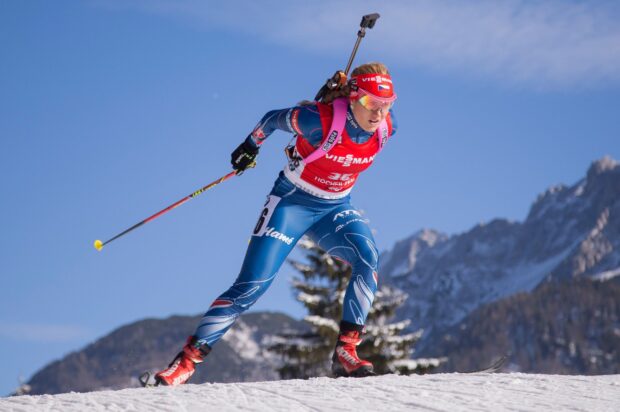 Female biathlon athlete skiing fast on snowy mountain terrain