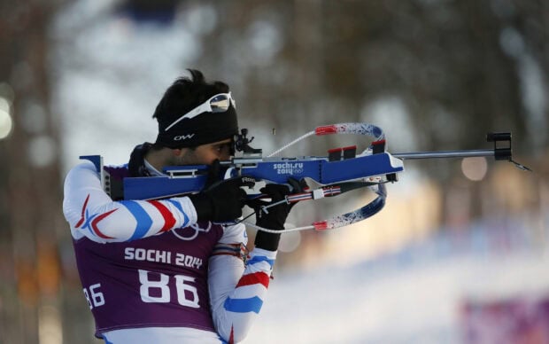 A biathlon athlete aiming a rifle during a winter competition at Sochi 2014