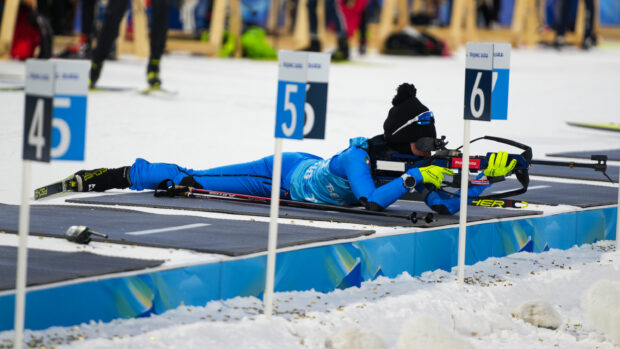 Athlete in blue gear aiming with rifle during biathlon competition on snow