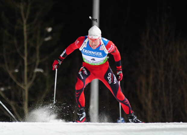 A biathlon athlete wearing red gear skiing fast on snow during a competition