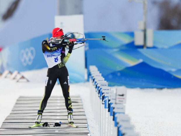 Biathlon athlete aiming with a rifle during a winter skiing competition in snowy conditions