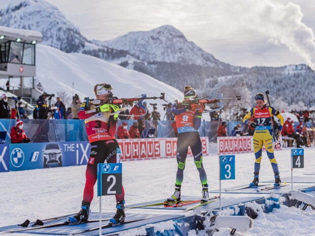 Three biathlon athletes aiming rifles during winter sports competition