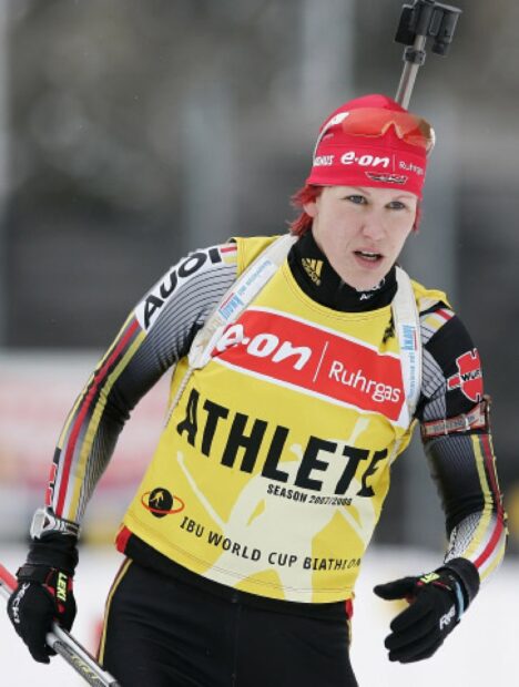 Female biathlon athlete skiing with red cap and yellow bib during competition