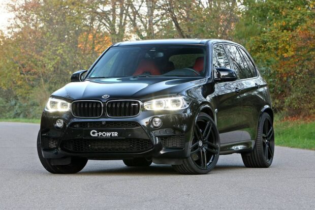 A black BMW X5 with illuminated headlights stands on a road surrounded by autumn trees, HD Desktop Wallpaper