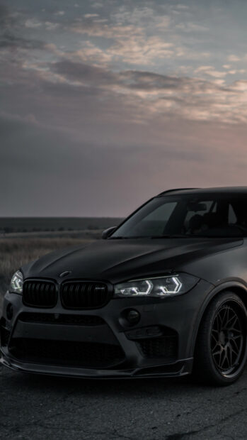 A sleek black BMW X5 is parked on an empty road at dusk with illuminated headlights, 4K Mobile Wallpaper