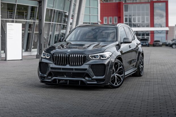 A black BMW X5 stands outside a modern glass building on a paved area, 2K Desktop Wallpaper