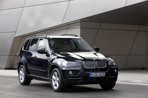 A black Bmw X5 is parked in front of a modern geometric building facade in this image, 2K Desktop Wallpaper