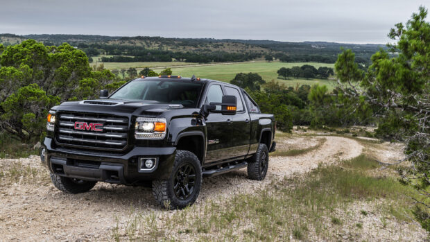 A black GMC truck is parked on a winding dirt path surrounded by green trees and hills, 4K Desktop Wallpaper
