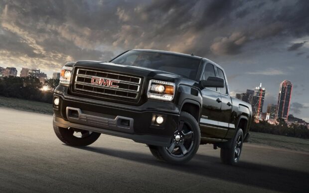 A black GMC truck is parked on a road with a city skyline and cloudy sky in the background, 2K Desktop Wallpaper