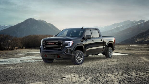A black GMC truck stands on rocky ground with mountains in the background, 4K Desktop Wallpaper