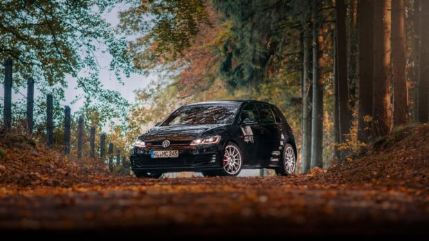 Một chiếc Golf Gti màu đen đỗ trên con đường rừng phủ đầy lá, xung quanh là cây cối, Hình nền máy tính HD