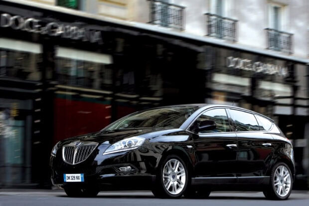 A black Lancia car is parked in front of a building in an urban area, 2K Desktop Wallpaper