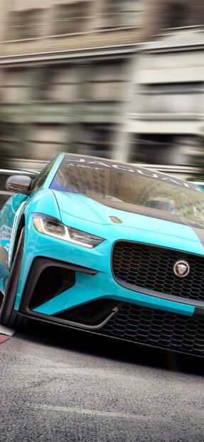 A blue Jaguar I Pace is racing fast through an urban area with blurred buildings in the background, 2K Mobile Wallpaper
