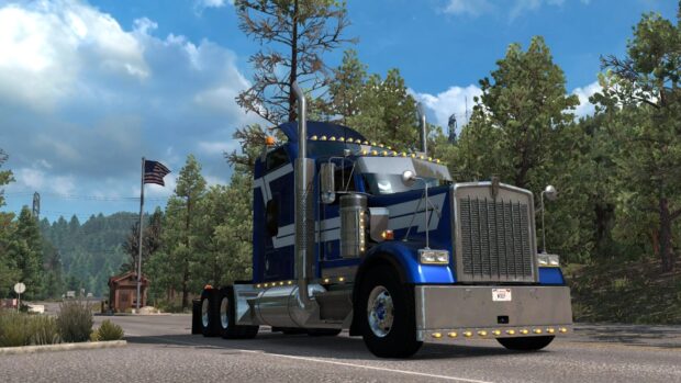 A blue Kenworth truck is parked beside a forest with an American flag visible in the background, HD Desktop Wallpaper