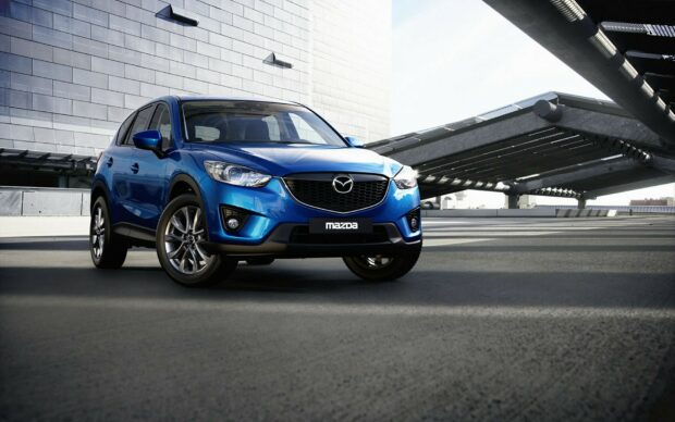 A blue Mazda SUV is parked outside a modern building with a sleek architectural design, displaying its front view, Mazda Wallpapers, HD Desktop Wallpaper