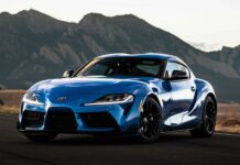 Blue Toyota Supra sports car on mountain road at sunset.