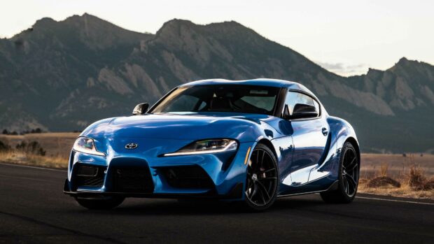 Blue Toyota Supra sports car on mountain road at sunset.