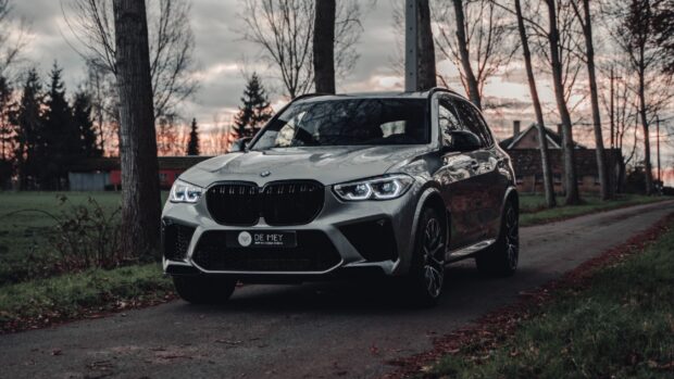 A silver Bmw X5 driving on a country road surrounded by trees in the evening, 4K Desktop Wallpaper