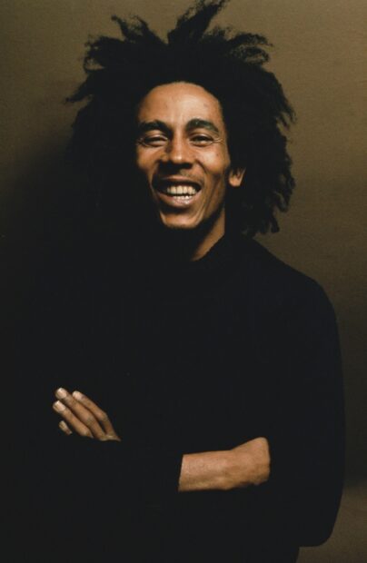 A joyful portrait of Bob Marley with crossed arms and natural hair, 2K Mobile Wallpaper
