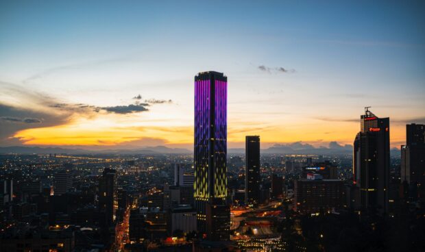 The Bogota skyline shows skyscrapers with colorful lights at sunset in a vibrant city scene, HD Desktop Wallpaper