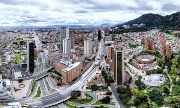 A panoramic view of Bogota city with tall buildings and surrounding mountains on a cloudy day, HD Desktop Wallpaper