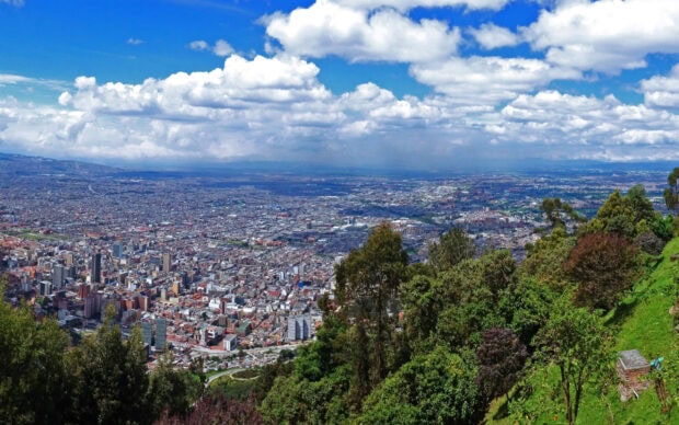A panoramic view of Bogota showcases the city blending with green hills under a blue sky, 2K Desktop Wallpaper