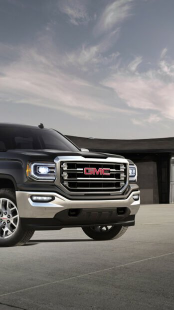 A bold GMC truck front grill is parked under a cloudy sky, showcasing design details on a smooth road, HD Phone Wallpaper