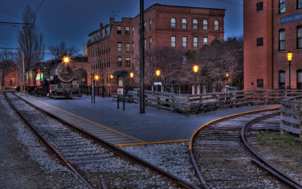 Historic Boston train on tracks near brick buildings at dusk with glowing street lamps