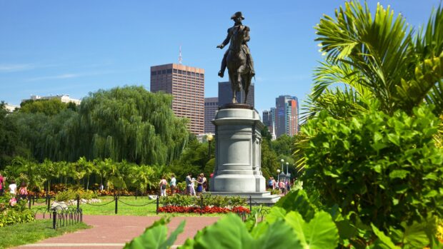 Statue of a man on horseback in a green park area with Boston city skyline in the background