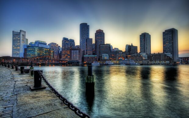 The Boston skyline at sunset with calm harbor waters and city lights reflecting on the surface