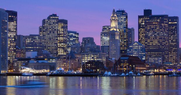 Boston city skyline at dusk with illuminated buildings reflected on the water