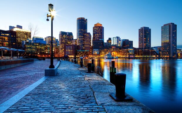 Evening view of Boston city skyline along the waterfront with illuminated buildings and clear sky