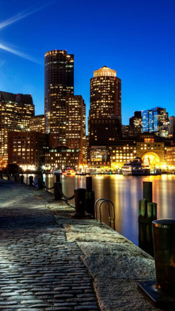 Boston waterfront with tall buildings lit at night along the harbor walkway