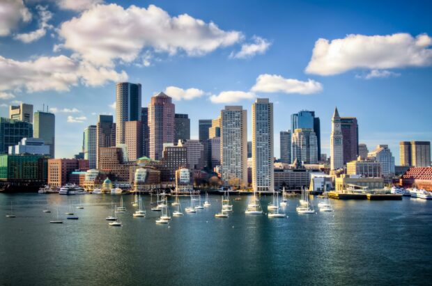 Boston skyline with sailboats floating on the calm harbor water under a blue sky with clouds