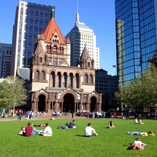 People relaxing on green lawn in Boston with historic church and modern buildings in background