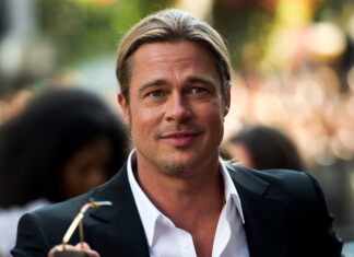 Brad Pitt smiling in a black suit jacket and white shirt outdoors