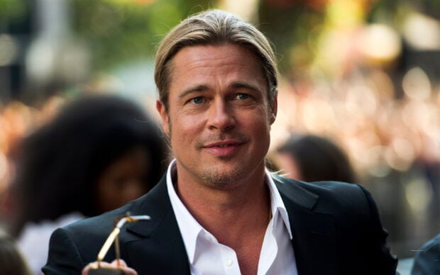 Brad Pitt smiling in a black suit jacket and white shirt outdoors